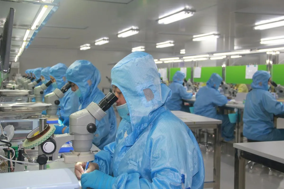 A close-up of a semiconductor wafer being handled by a robotic arm in a cleanroom factory environment.