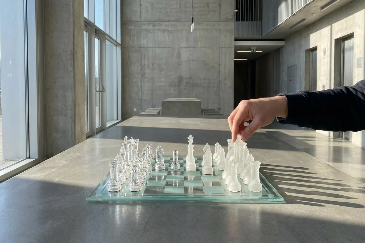Glass chess set on a concrete table under bright light.