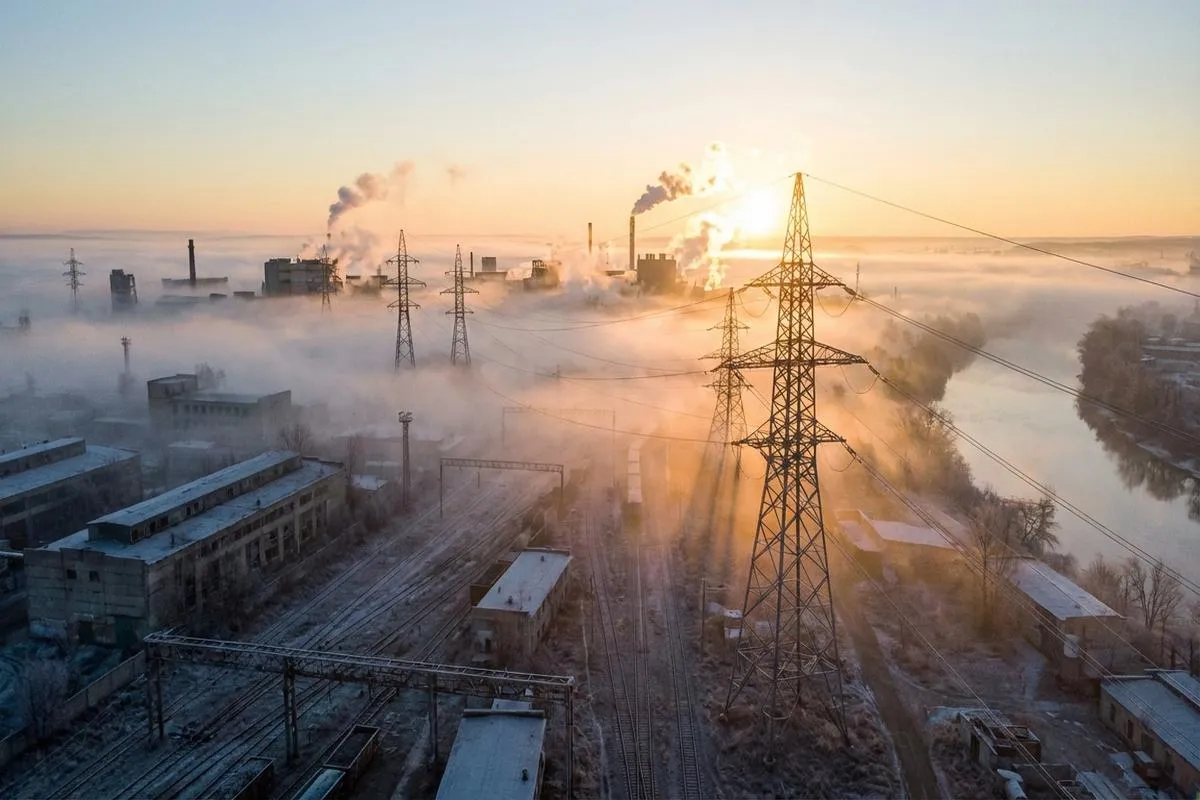 High-voltage transmission lines in a foggy industrial landscape at dawn.